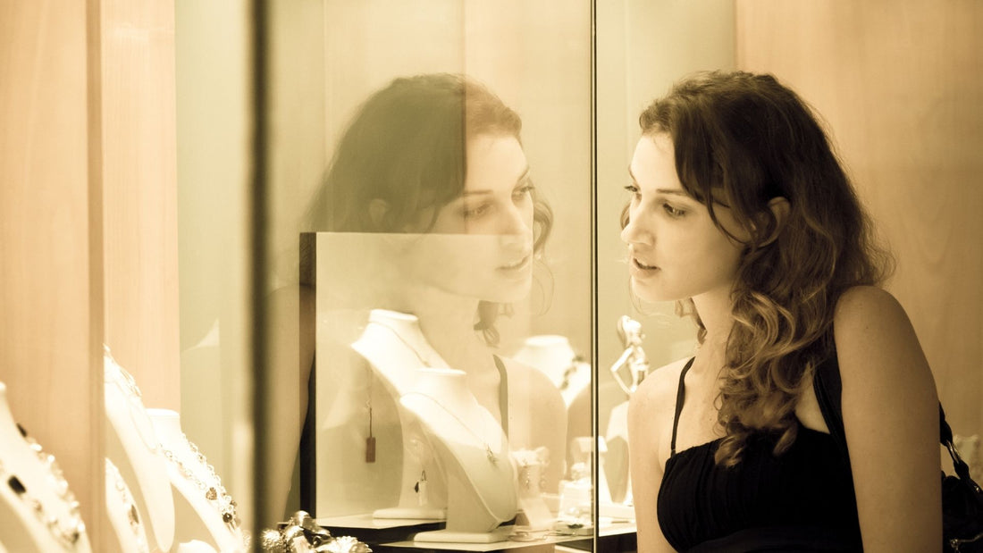 Woman inspecting fine jewellery in a sunlit boutique display, illustrating a thoughtful jewellery shopping visit