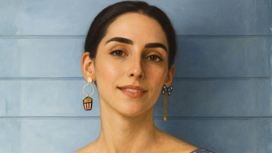 Portrait of a woman with styled hair wearing delicate mismatched gold earrings against a pale blue backdrop