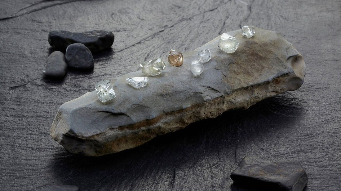 Rough diamond stones and a pale mineral crystal against a charcoal surface