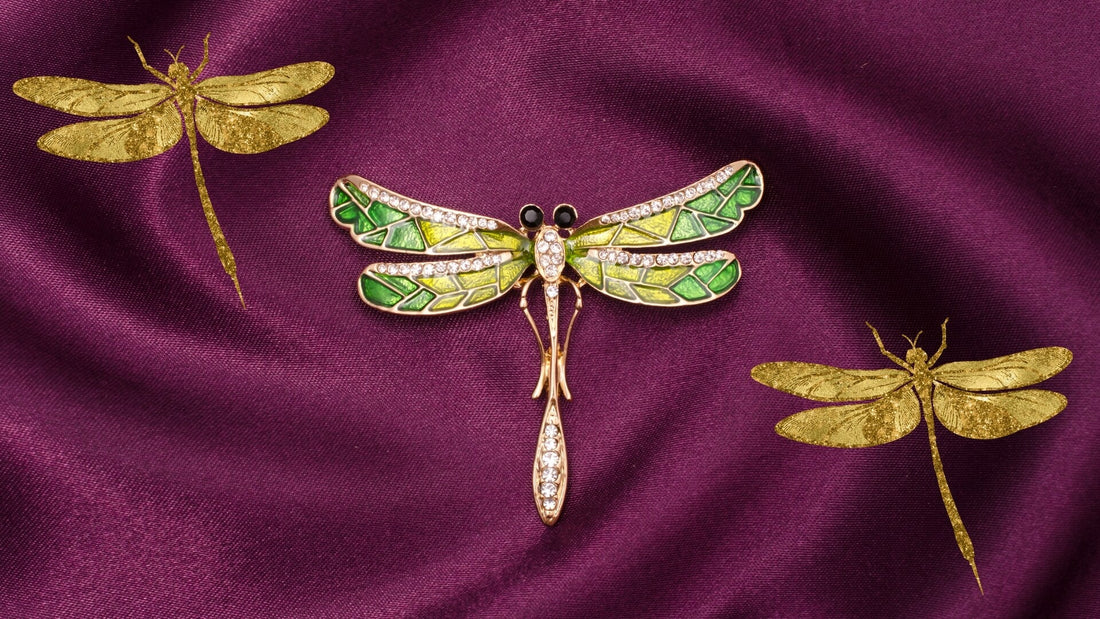 Three dragonfly-shaped jewellery pieces with green and gold wings on a burgundy background