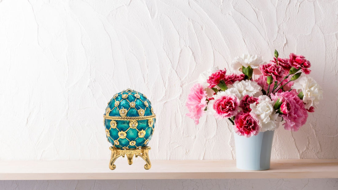 Ornate turquoise and gold Fabergé-style egg beside a vase of pink flowers