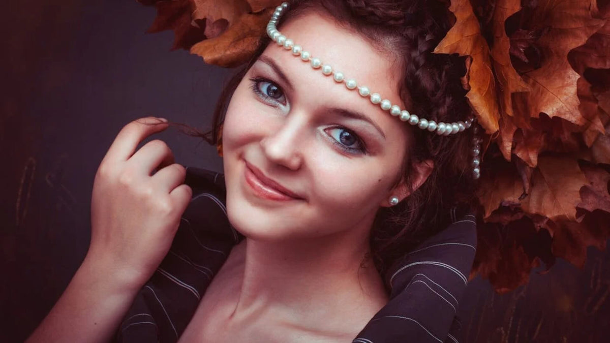 Woman with copper-red hair in an autumn setting, wearing jewellery and smiling softly