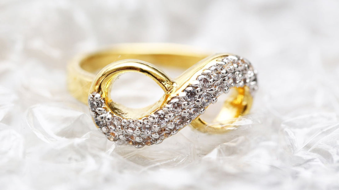 Intertwined gold and diamond infinity rings resting on light marble