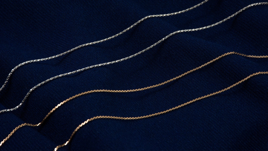 Fine gold and silver necklaces layered over a dark navy surface to illustrate mixed metals