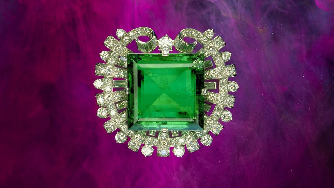 Rectangular green emerald brooch surrounded by diamonds on a rich purple background