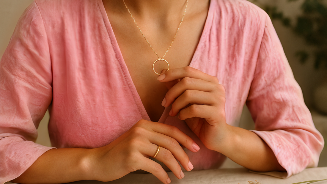 Close-up of a gold circular pendant and delicate necklace worn with a pink top, symbolising eternity and connection