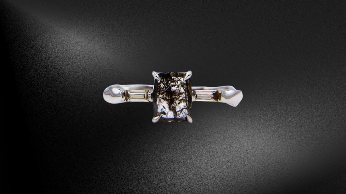 Close-up of a silver ring set with a dark salt-and-pepper diamond on a black background