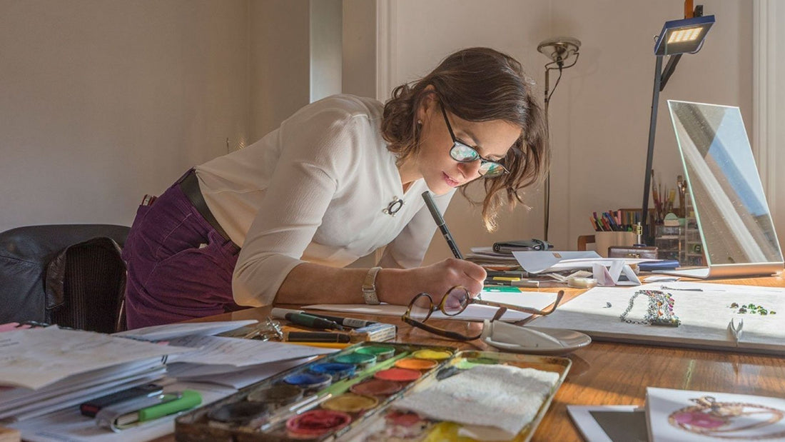 Jewellery artist painting a detailed design at a workshop desk, demonstrating gouache artwork