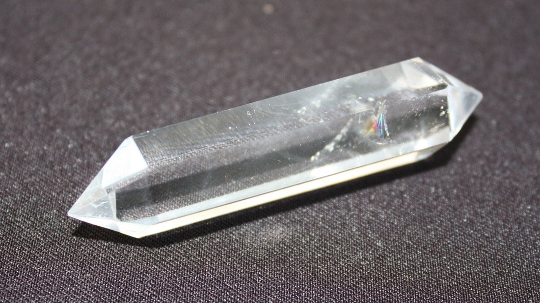 Transparent pointed clear quartz crystal resting on a textured grey surface, showing its natural faceted shape