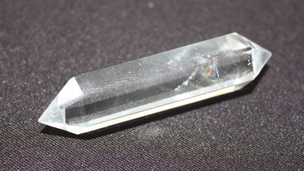Transparent pointed clear quartz crystal resting on a textured grey surface, showing its natural faceted shape