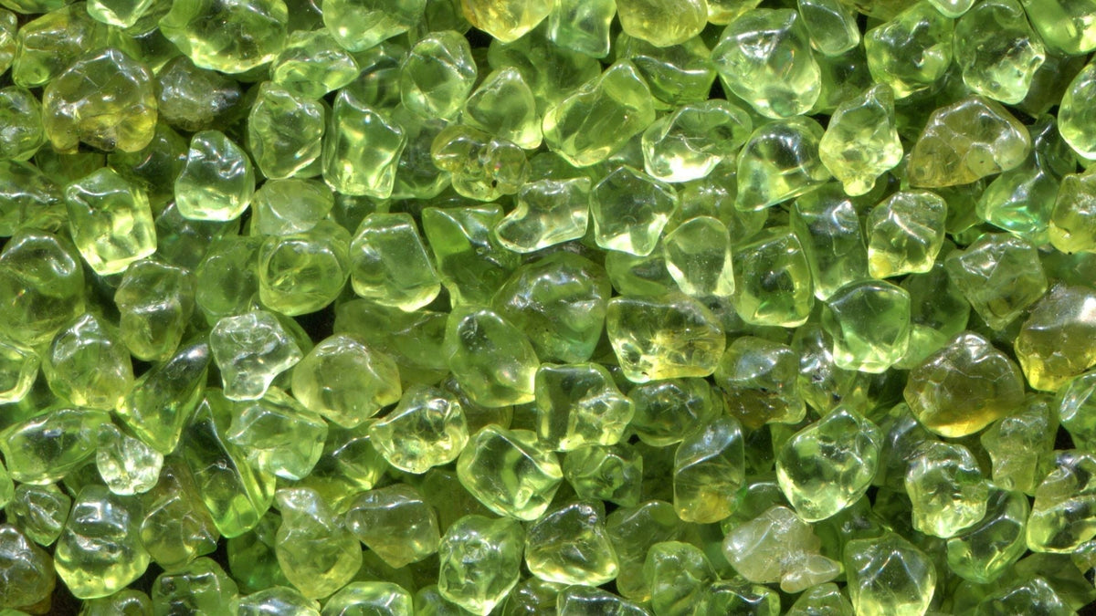 Small bright lime-green peridot gemstones scattered together, glowing in natural light