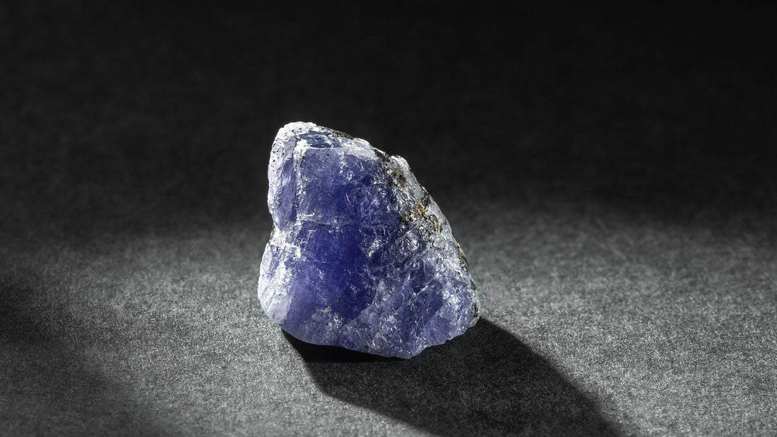 Rough violet-blue tanzanite crystal displayed on a dark textured surface in close-up