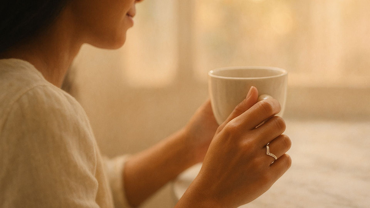 Woman holding a white coffee cup while wearing a slender chevron-shaped gold ring on her finger