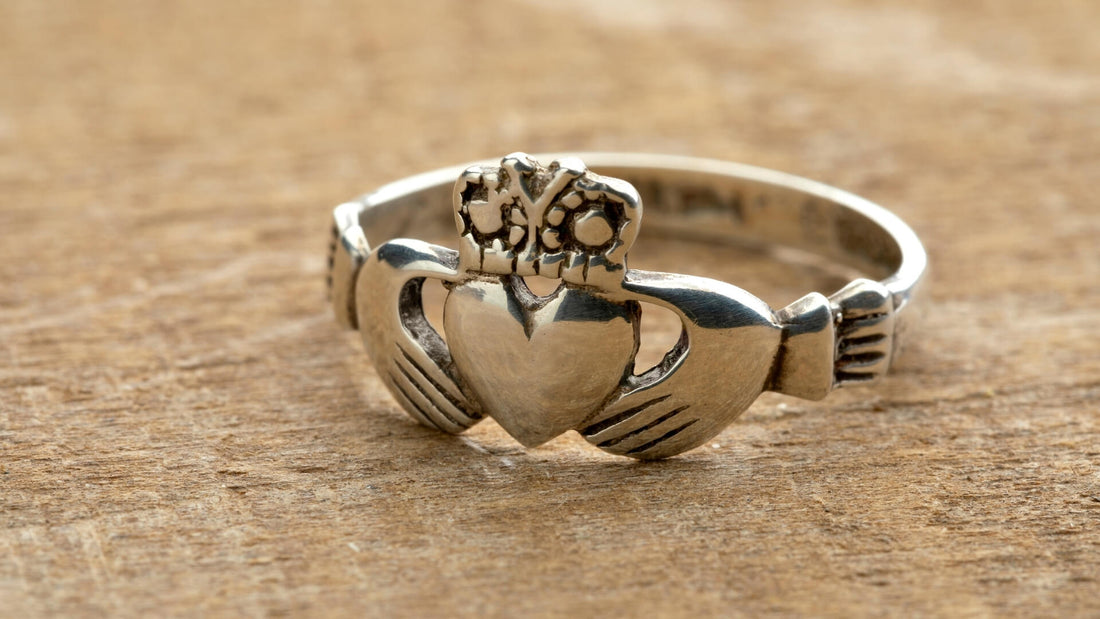 Silver Claddagh ring with crowned heart and clasped hands photographed on a sandy stone surface
