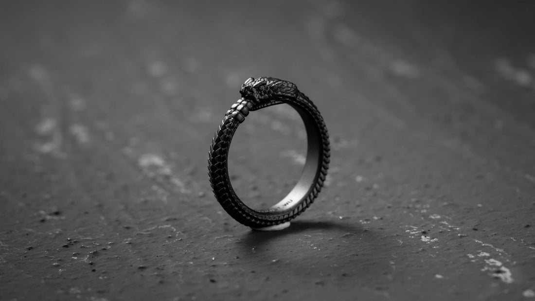 Dark circular ouroboros snake ring photographed against textured grey stone