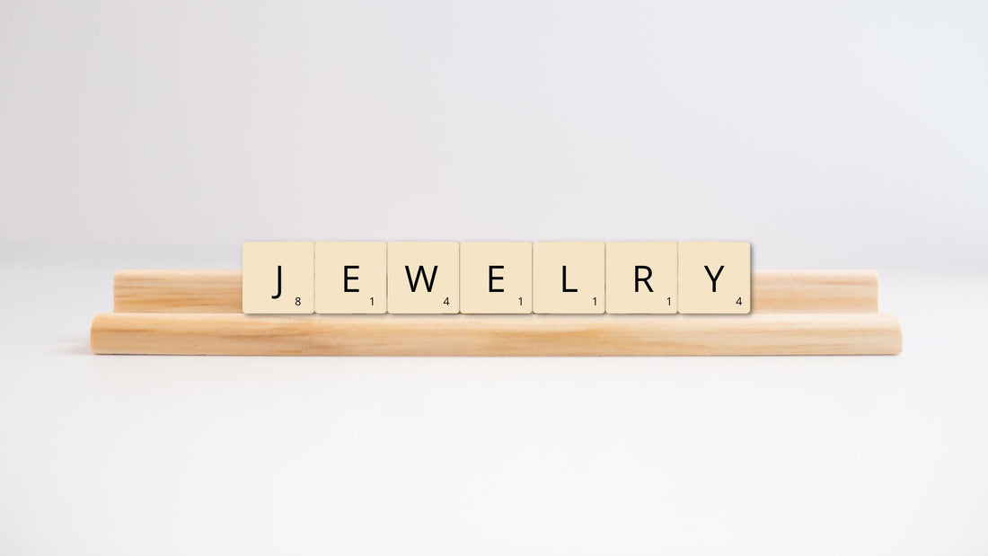 Wooden letter tiles spelling jewellery alongside a simple gold chain on a white background