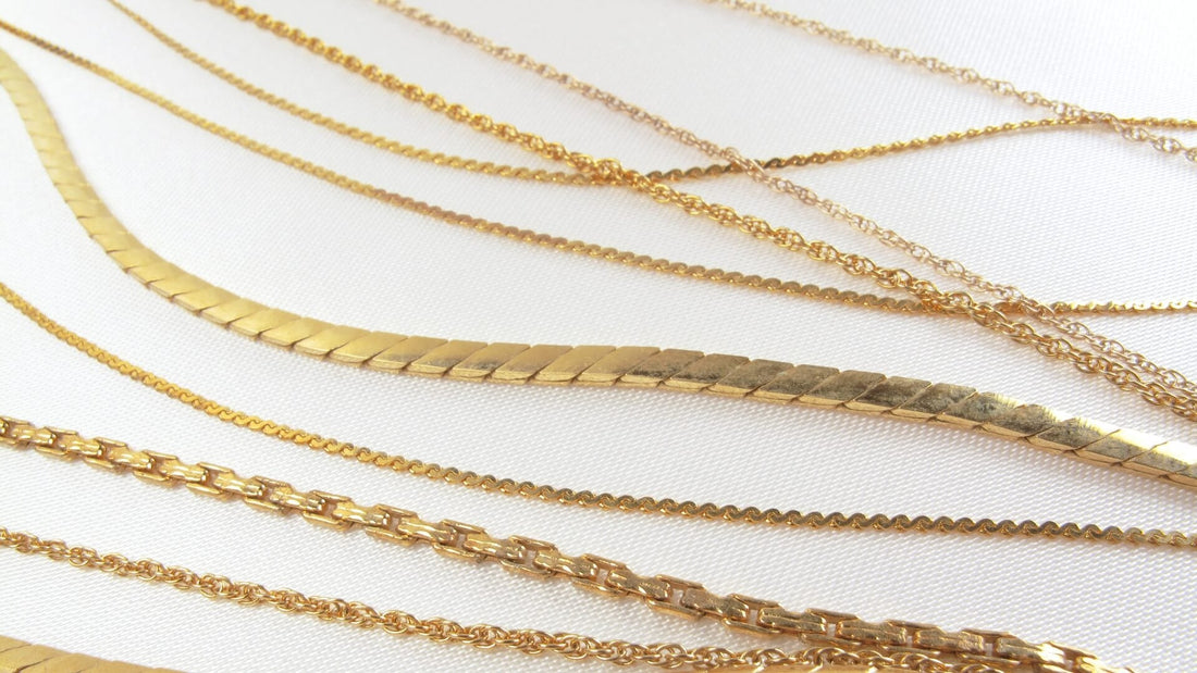 Delicate permanent gold chains displayed on a deep navy fabric background